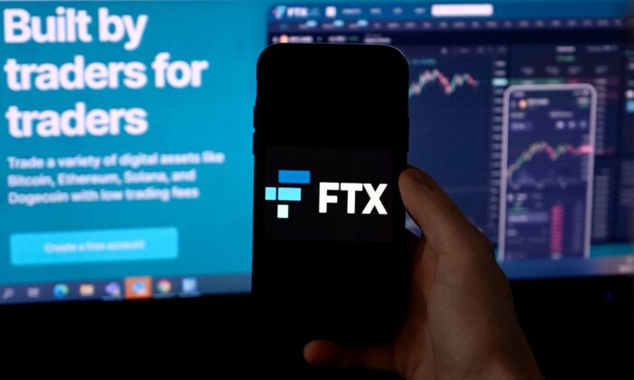 Màn hình điện thoại thông minh hiển thị logo của nền tảng giao dịch mã kim FTX, với màn hình hiển thị trang web FTX trên nền ở Arlington, Virginia, hôm 10/02/2022. (Ảnh: Olivier Douliery/AFP/Getty Images)