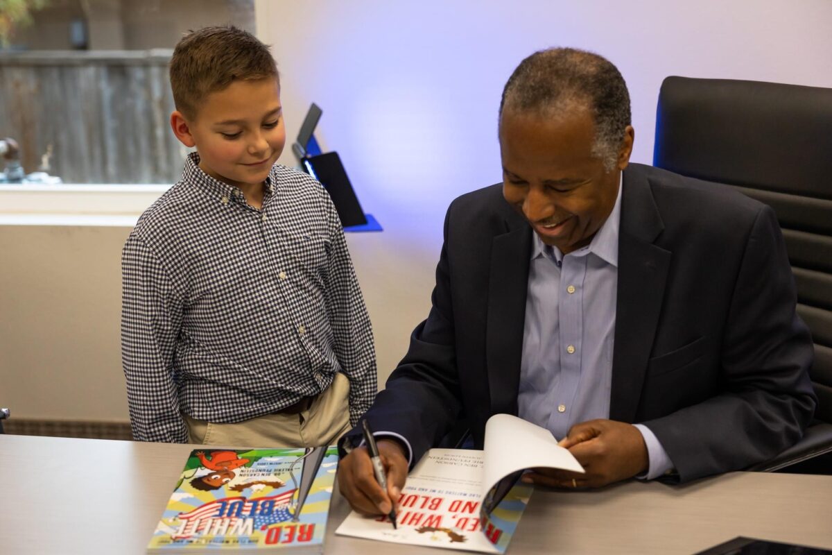 Cho đến nay, Bác sĩ Ben Carson đã phát hành hai cuốn sách dành cho trẻ em để bổ sung vào chương trình giảng dạy do Viện Cornerstone Mỹ quốc cung cấp. Bức ảnh này chụp ông ở tại trụ sở chính của Patriot Mobile vào tháng 11/2022 trong một buổi ký tặng sách cho cuốn sách “Red, White and Blue Our Flag Matters to Me and You” (Đỏ, Trắng, Và Xanh — Lá Cờ Của Chúng Ta Quan Trọng Đối Với Tôi Và Bạn). (Ảnh: Đăng dưới sự cho phép của Viện Cornerstone Mỹ quốc)