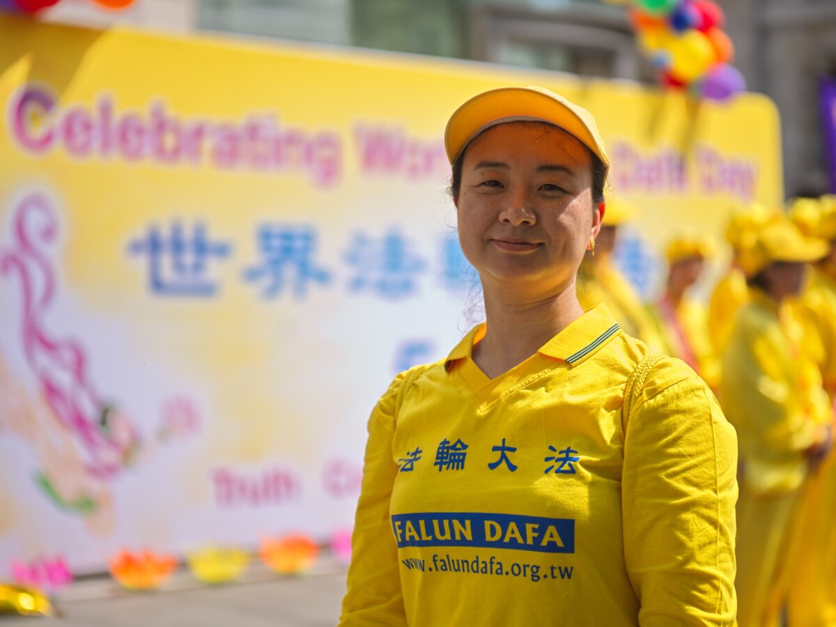 Một học viên Pháp Luân Công đứng trước tấm biểu ngữ trong sự kiện thường niên kỷ niệm Ngày Pháp Luân Đại Pháp Thế giới tại London, hôm 11/05/2024. (Ảnh: Yanning Qi/The Epoch Times)