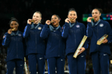 Cô Simone Biles (trái) và đồng đội của đội tuyển Hoa Kỳ chụp hình với huy chương vàng trong lễ trao giải cho trận chung kết đồng đội nữ môn thể dục dụng cụ nghệ thuật trong Thế vận hội Paris 2024, tại Nhà thi đấu Bercy ở Paris, hôm 30/07/2024. (Ảnh của Lionel Bonaventure/AFP)